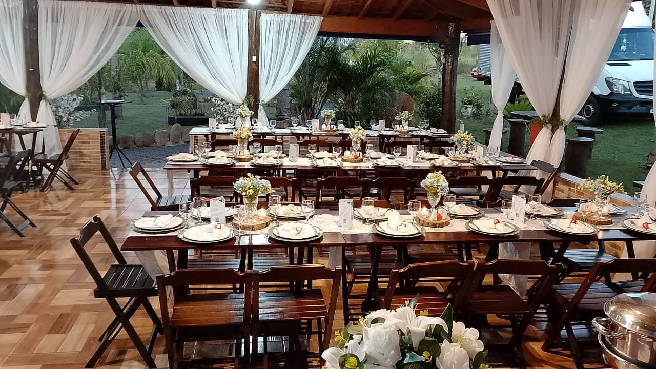 Salão de festas decorado com mesas postas, cortinas brancas e arranjos de flores